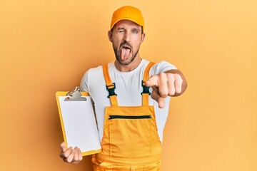 Sticker - Young handsome man wearing courier uniform holding clipboard sticking tongue out happy with funny expression.