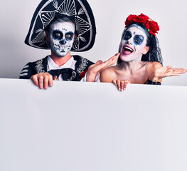 Sticker - Young couple wearing mexican day of the dead costume holding blank empty banner pointing aside with hands open palms showing copy space, presenting advertisement smiling excited happy