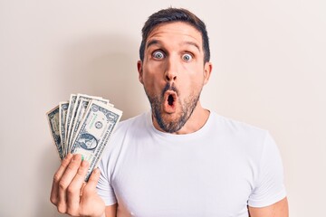 Sticker - Young handsome man holding bunch of dollars banknotes over isolated white background scared and amazed with open mouth for surprise, disbelief face