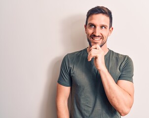 Canvas Print - Young handsome man wearing casual t-shirt standing over isolated white background smiling looking confident at the camera with crossed arms and hand on chin. Thinking positive.