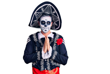 Poster - Young man wearing day of the dead costume over background praying with hands together asking for forgiveness smiling confident.