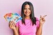 Young latin girl holding swiss franc banknotes smiling happy pointing with hand and finger to the side