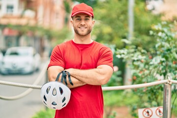 Sticker - Young caucasian deliveryman smiling happy holding bike helmet at the city.