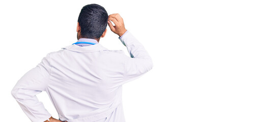 Wall Mural - Young hispanic man wearing doctor uniform and stethoscope backwards thinking about doubt with hand on head