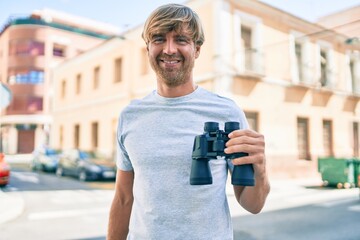 Sticker - Young irish man smiling happy using binoculars at street of city.