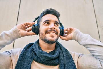 Young hispanic man smiling happy listening to music using headphones at the city.