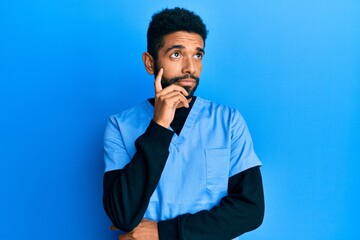 Sticker - Handsome hispanic man with beard wearing blue male nurse uniform serious face thinking about question with hand on chin, thoughtful about confusing idea