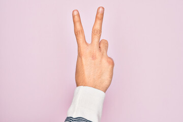 Hand of caucasian young man showing fingers over isolated pink background counting number 2 showing two fingers, gesturing victory and winner symbol