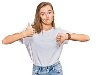 Beautiful young blonde woman wearing casual white t shirt doing thumbs up and down, disagreement and agreement expression. crazy conflict