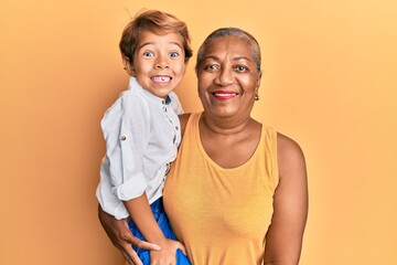 Poster - Hispanic grandson and grandmother together over yellow background looking positive and happy standing and smiling with a confident smile showing teeth