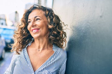 Poster - Middle age hispanic woman smiling happy leaning on the wall at the city.