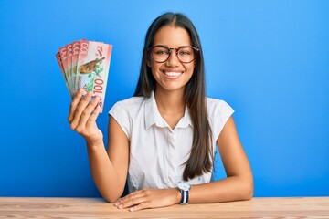 Canvas Print - Beautiful hispanic woman holding 100 new zealand dollars banknote looking positive and happy standing and smiling with a confident smile showing teeth