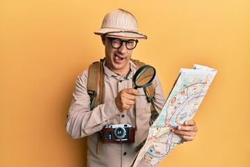 Wall Mural - middle age bald man wearing explorer hat holding magnifying glass on a map winking looking at the ca