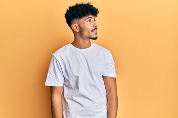 Young arab handsome man wearing casual white tshirt looking to side, relax profile pose with natural face and confident smile.