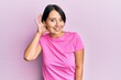 © Krakenimages.com - Beautiful young woman with short hair wearing pink tshirt over pink background smiling with hand over ear listening and hearing to rumor or gossip. deafness concept.
