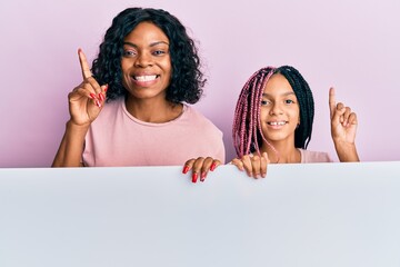 Poster - Beautiful african american mother and daughter holding blank empty banner smiling with an idea or question pointing finger with happy face, number one