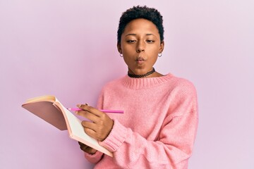 Wall Mural - Young african american girl reading and writing book making fish face with mouth and squinting eyes, crazy and comical.