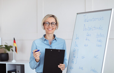 Online schooling. Positive German teacher posing near blackboard with grammar rules, looking at camera and smiling