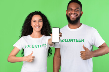 Wall Mural - Two Volunteers Showing Phone Empty Screen Gesturing Like, Green Background