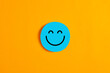 Blue round circle with a happy or smiley face icon on it against yellow background.