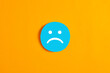 © Cagkan - Blue round circle with a sad face icon against yellow background.