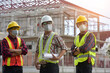 © saravut - Construction engineers supervising progress of construction project stand on new factory,Engineering Consulting People on construction site holding blueprint in his hand.