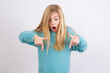 Amazed Cute Caucasian kid girl wearing blue knitted sweater against white wall points down with fore fingers, opens mouth being shocked. Advertisement concept.