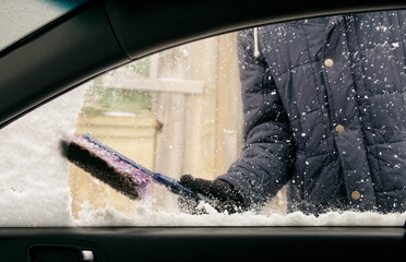 Wall Mural - Male driver with gloves brushes snow off passenger side window of car - view from passenger compartment