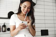 Lifestyle. Beautiful Asian Woman Brushing Teeth And Reading Message On Phone From Bathroom. Girl With Smartphone Using Toothbrush, Checking Social Networks