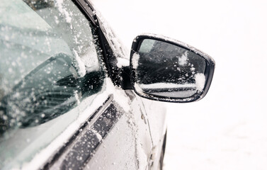 The grey car's cleaned mirror is dusted with snow on the street