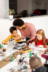 Wall Mural - African American female science teacher with group of kids programming electric toys and robots at robotics classroom