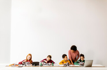 happy kids with their african american female science teacher with laptop programming electric toys 