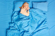 © wayhome.studio  - Peaceful pleased mature woman enjoys good healthy sleep poses in cozy bed with blue bedclothes wears pajamas lies with closed eyes spends lazy weekend at home. Above top view. Falling asleep