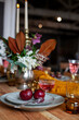 © Dana Keli - long wooden party table with stylish decoration, with candlesticks, vases of flowers, glasses with wine, plates and food in a room with a white brick wall