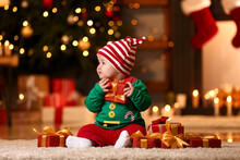 Cute Little Baby In Elf's Costume And With Gifts At Home On Christmas Eve