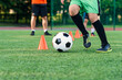 © gorynvd - Close up boy in sportswear trains football on soccer field and learns to circle the ball between training orange cones.