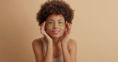pretty natural dark skinned female model applies hydrogel patches uder eyes for healthy skin has cur