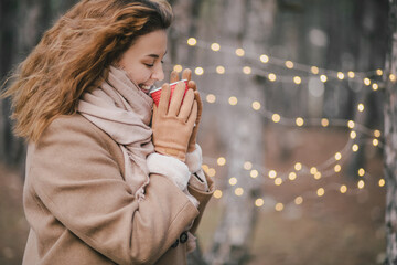 Young beautiful woman enjoying coffee to go with golden festive lights on a background.