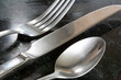 A close up view of a fork, knife and spoon flatware laying on a black granite counter top