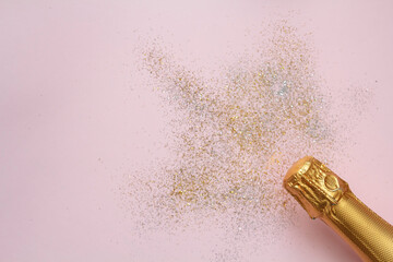 Champagne bottle and glitter on pink background with copy space. Top view, flat lay. Celebration concept