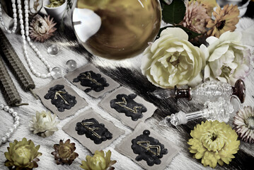 Styled still life with black runes, magic ball, yellow flowers, candles and magic objects on witch table.