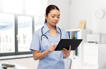 Wall Mural - medicine, profession and healthcare concept - asian female doctor or nurse in blue uniform with tablet pc computer and stethoscope over hospital background