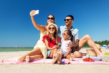 Poster - family, leisure and people concept - father, mother and two little daughters taking selfie with smartphone on summer beach