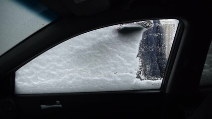 Wall Mural - Male driver in gloves brushes car windshield from snow - view from interior