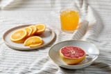 Fototapeta Kuchnia - food, healthy eating and fruits concept - still life of grapefruit, sliced orange and glass of juice over drapery