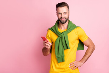 Wall Mural - Photo of cute young guy wear yellow t-shirt pullover shoulders holding modern device empty space isolated pink color background