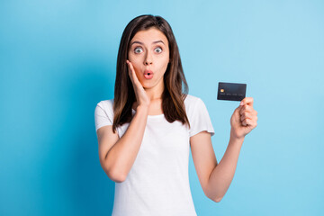 Sticker - Photo of young shocked amazed surprised girl hold hand cheek showing credit card isolated on blue color background