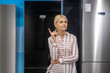 © zinkevych - Blonde woman in striped shirt choosing fridge in a showroom