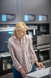 © zinkevych - Woman in striped shirt examining a washing machine in a showroom