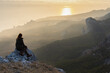 © Anna Pismenskova - A girl stands on a mountain and looks at the sunset. Atmospheric evening view of the mountains and the sea. beautiful aerial perspective. The concept of relaxation and meditation. Bright sunlight.